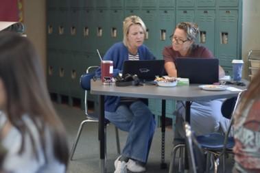 Two educators working together at a table with green lockers in the background.